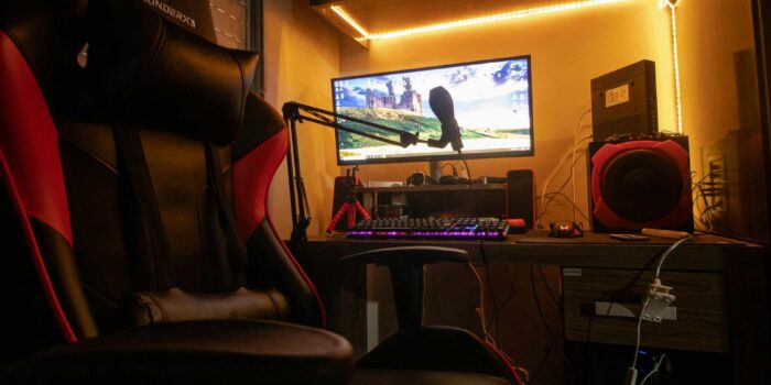 Patogi žaidimų kėdė su reguliuojamais porankiais ir nugaros atrama moderniame kambaryje.